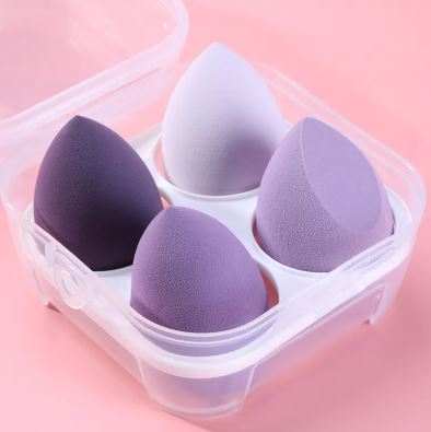 Le lot de 4 éponges de maquillage My Store, en différentes nuances violettes, est présenté dans un étui transparent sur fond rose, parfait pour une application précise et une finition impeccable.