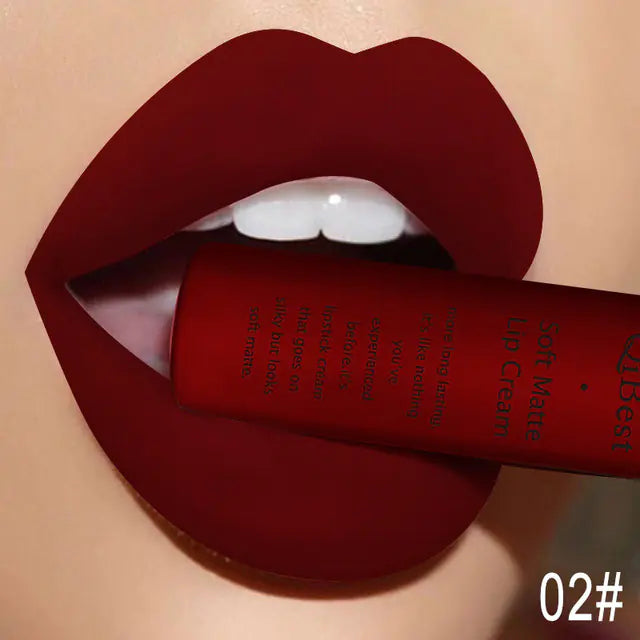 A close-up of lips in deep red Matte Non-Stick Liquid Lip Gloss - Long-Lasting Finish by Léa Beauty & Cosmetics, holding the gloss tube between the teeth. “02#” appears in the bottom right corner.