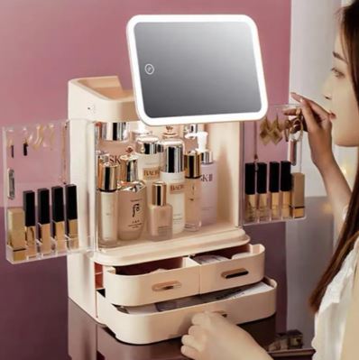 A woman sits at a vanity, organizing beauty products in the My Store Boîte de rangement à écran LED, a cream-colored organizer with drawers, side compartments, and an LED screen mirror on top.