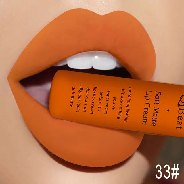 A close-up of lips wearing orange Léa Beauty & Cosmetics Matte Non-Stick Liquid Lip Gloss - Long-Lasting Finish, holding the labeled orange tube between the teeth. The image is marked 33# in the bottom right corner.
